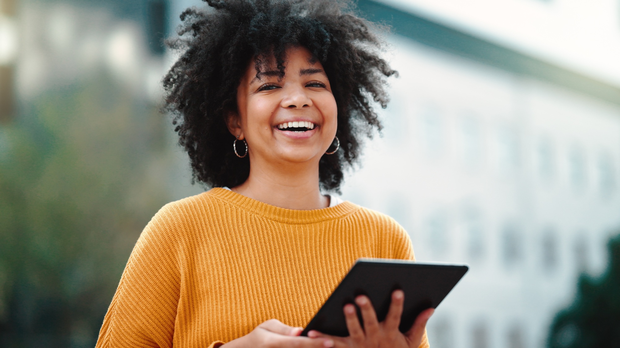 Portrait of happy woman with a digital tablet standing outside against a blurred urban background w